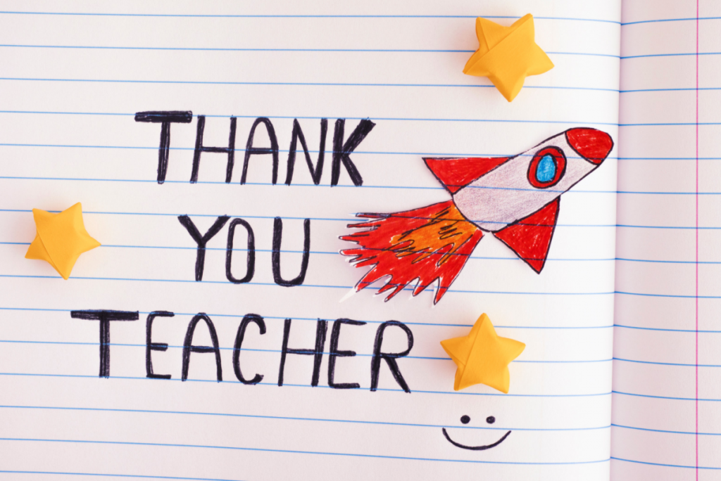 Thank you teacher writtern in child's handwriting in a notebook with lined paper. Has a hand drawn rocket in red and white and yellow stars on it